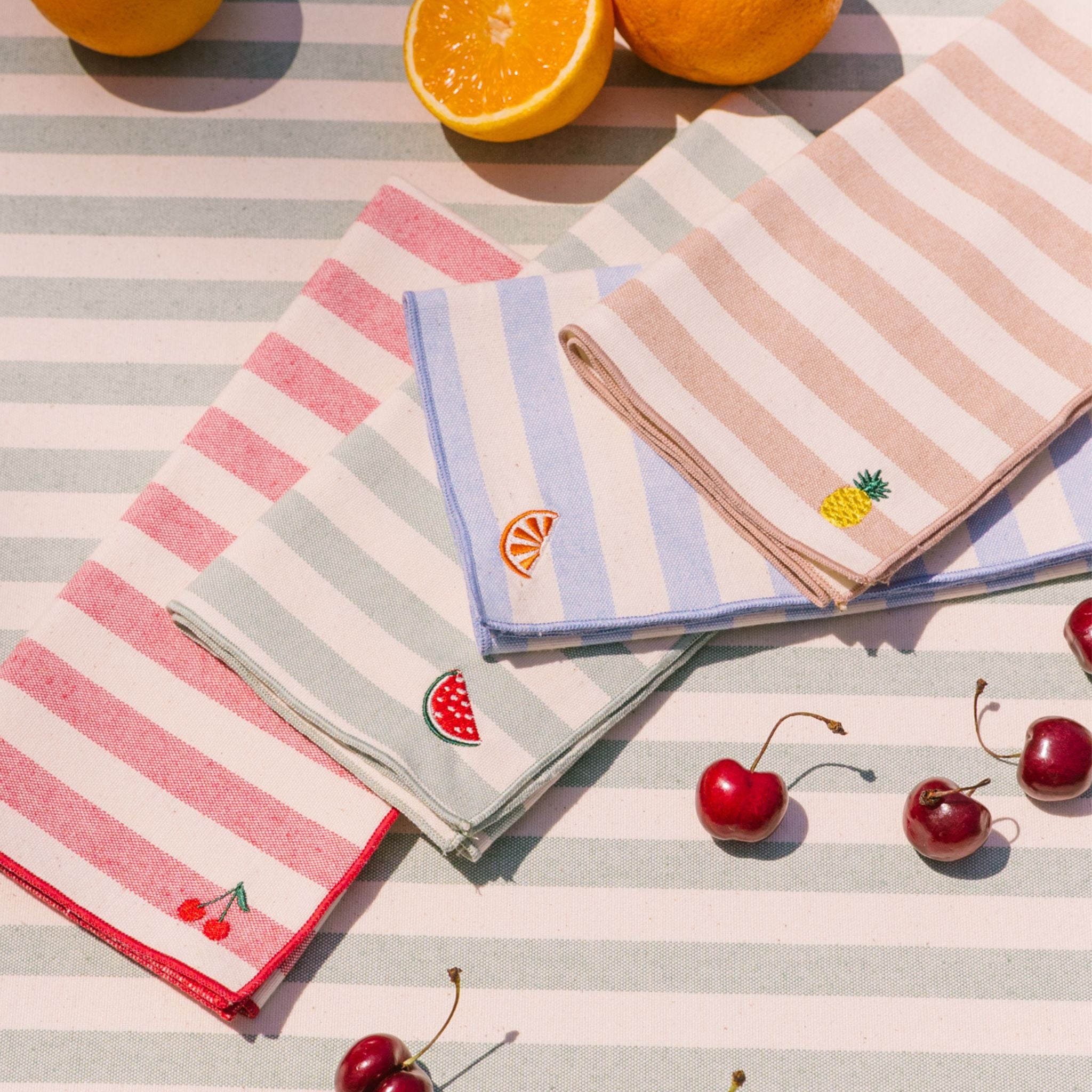 Set of striped napkins with fruit designs on a striped tablecloth.